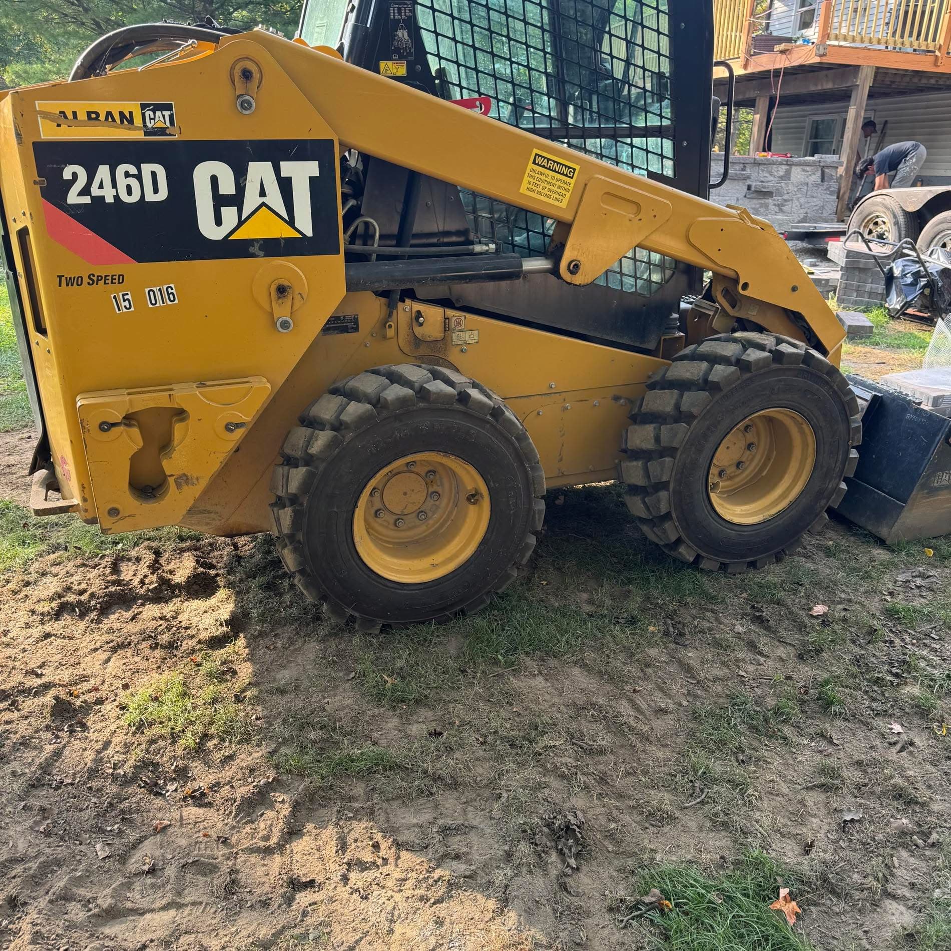 Yellow Caterpillar 246D skid steer loader parked on a dirt and grass construction site.